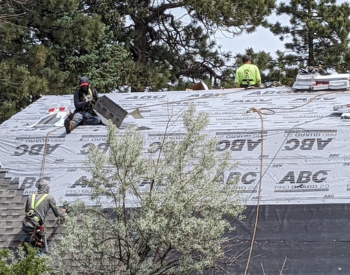 Roofing contractors installing GAF AS II Shingles on a Capitola home, working on a roof covered with protective underlayment, surrounded by trees.