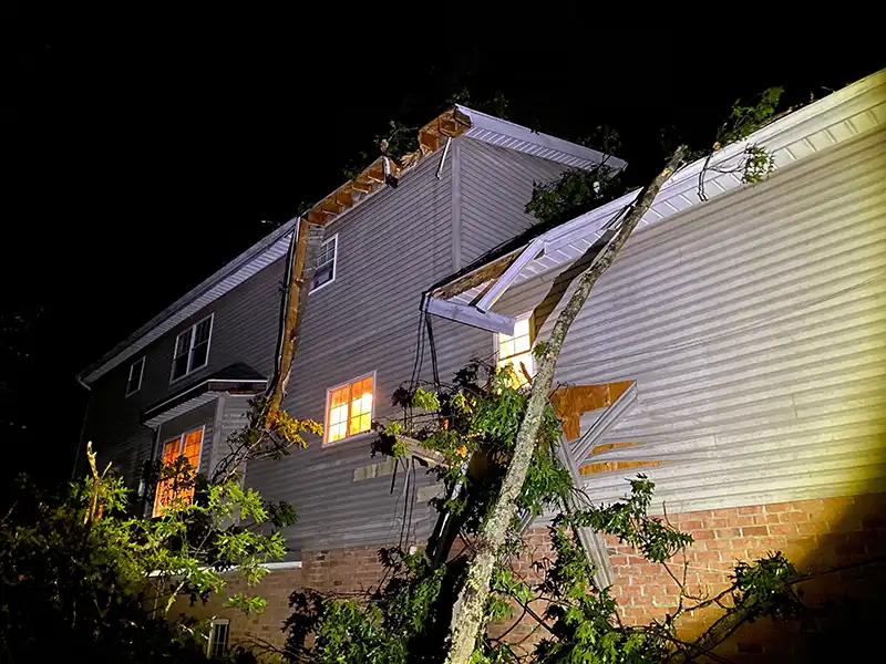Storm damaged home at night with broken soffits and gutters and small tree branches all over the exterior