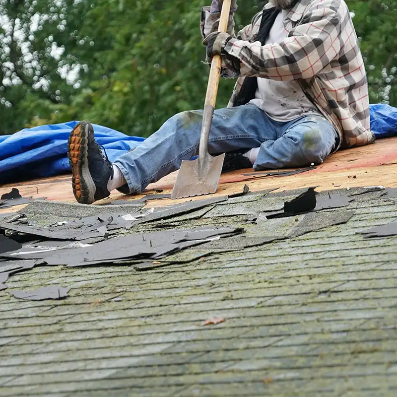 Roofer removing old, moldy shingles from a residential roof with a shovel